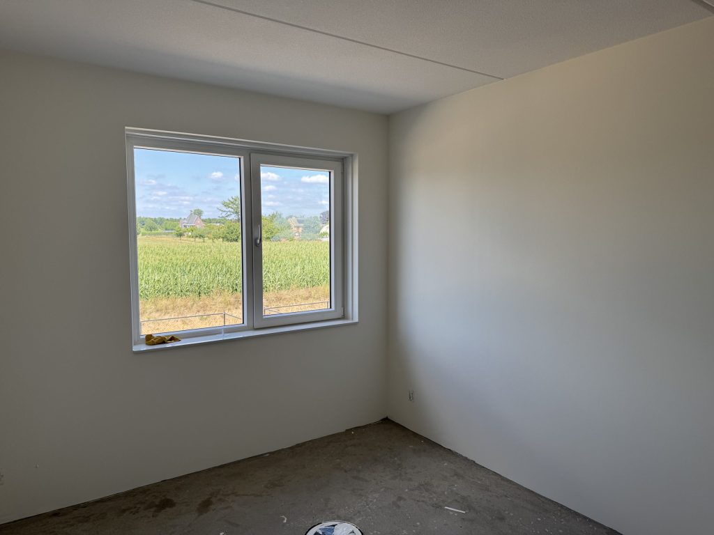 Lege kamer met strak afgewerkte, lichte wanden en een raam met uitzicht op het land