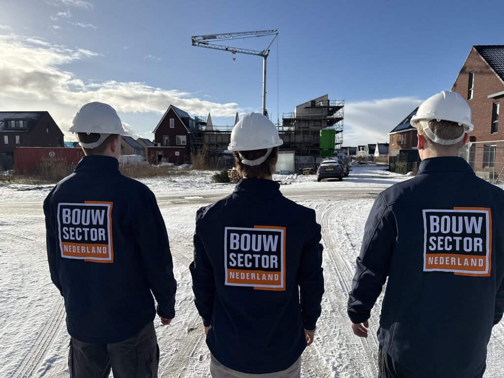 Drie vakmensen van Bouwsector Nederland met witte helm bij nieuwbouwwoningen in aanbouw in de sneeuw