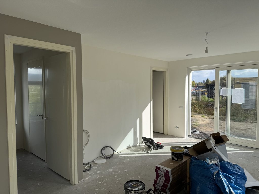 Nieuwbouwkamer met kale wanden en deuren naar slaapkamer en gang, vlak voor het behangen