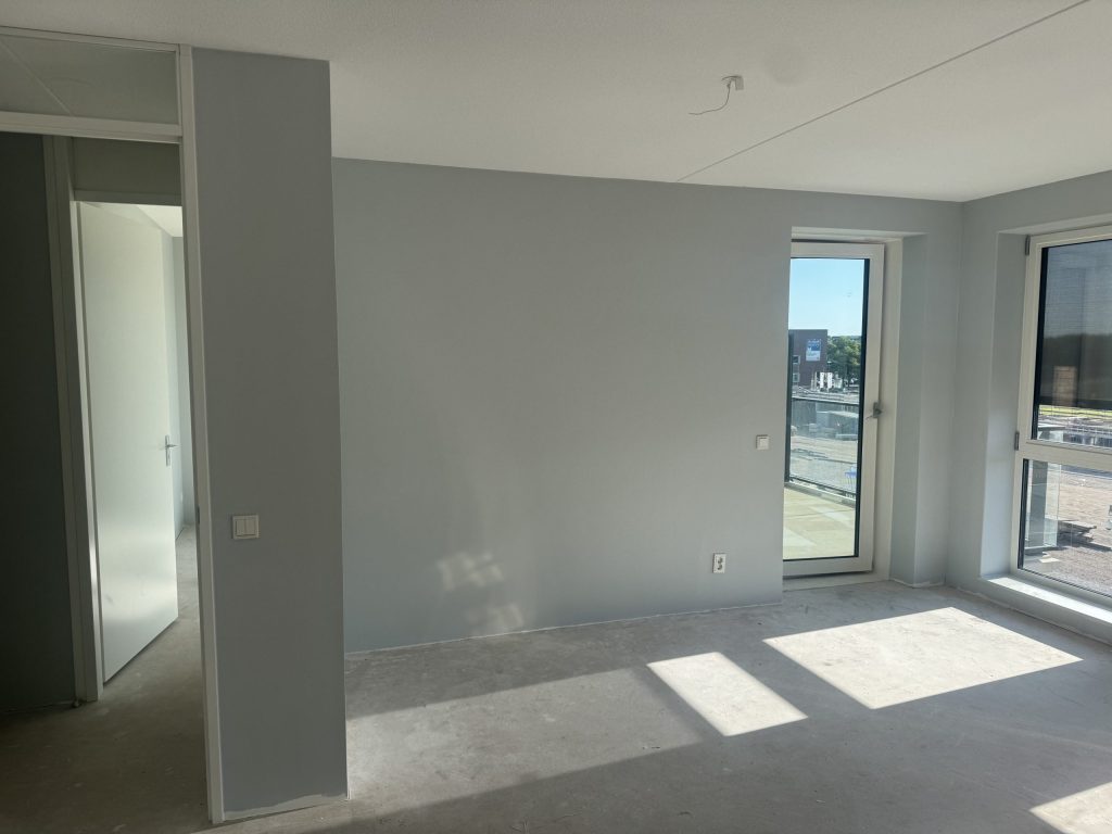 Appartement in aanbouw met een egaal afgewerkte grijze wand en een balkondeur