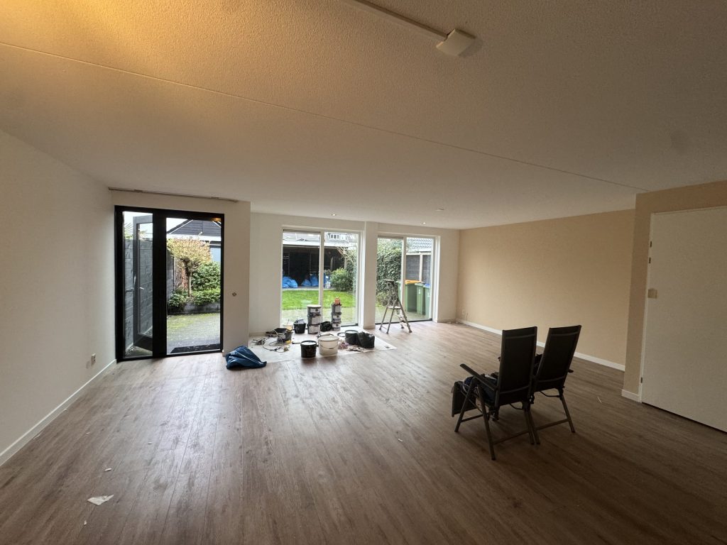 Lege woonkamer van een bestaand huis met tuindeuren, klaar voor nieuwe wandafwerking